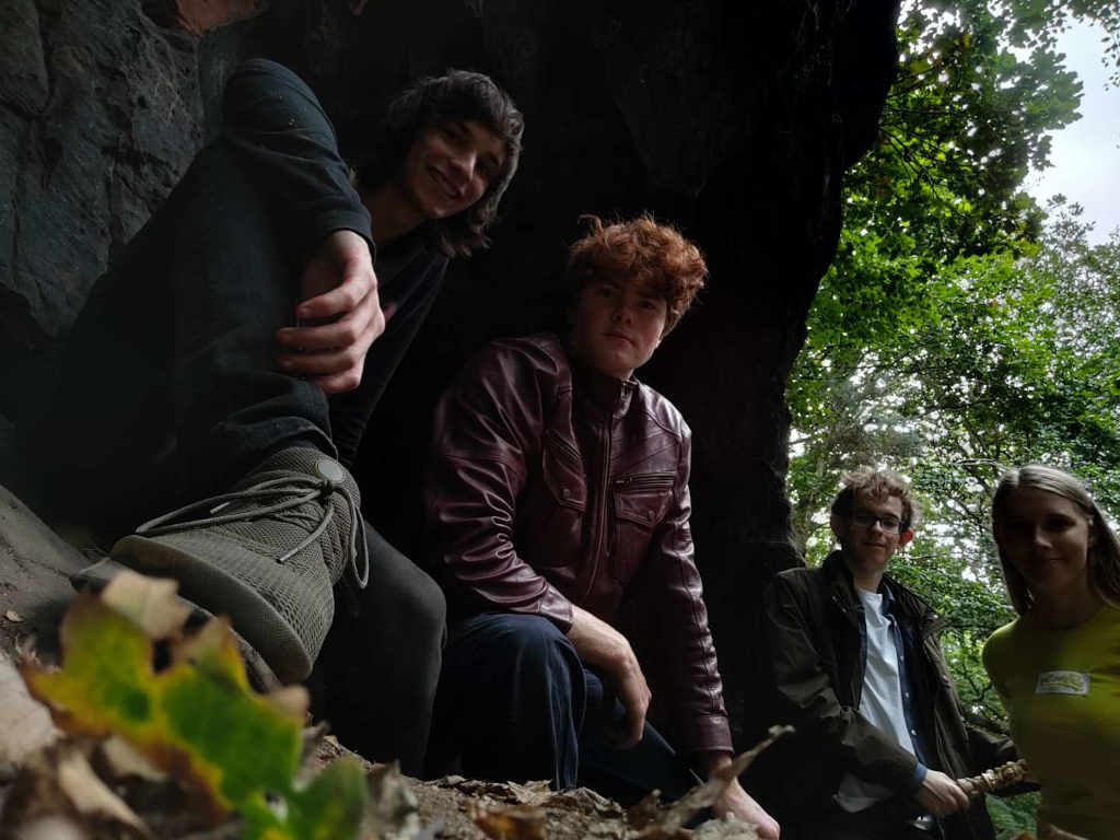 Four actors crouched in a cave on the cliffside