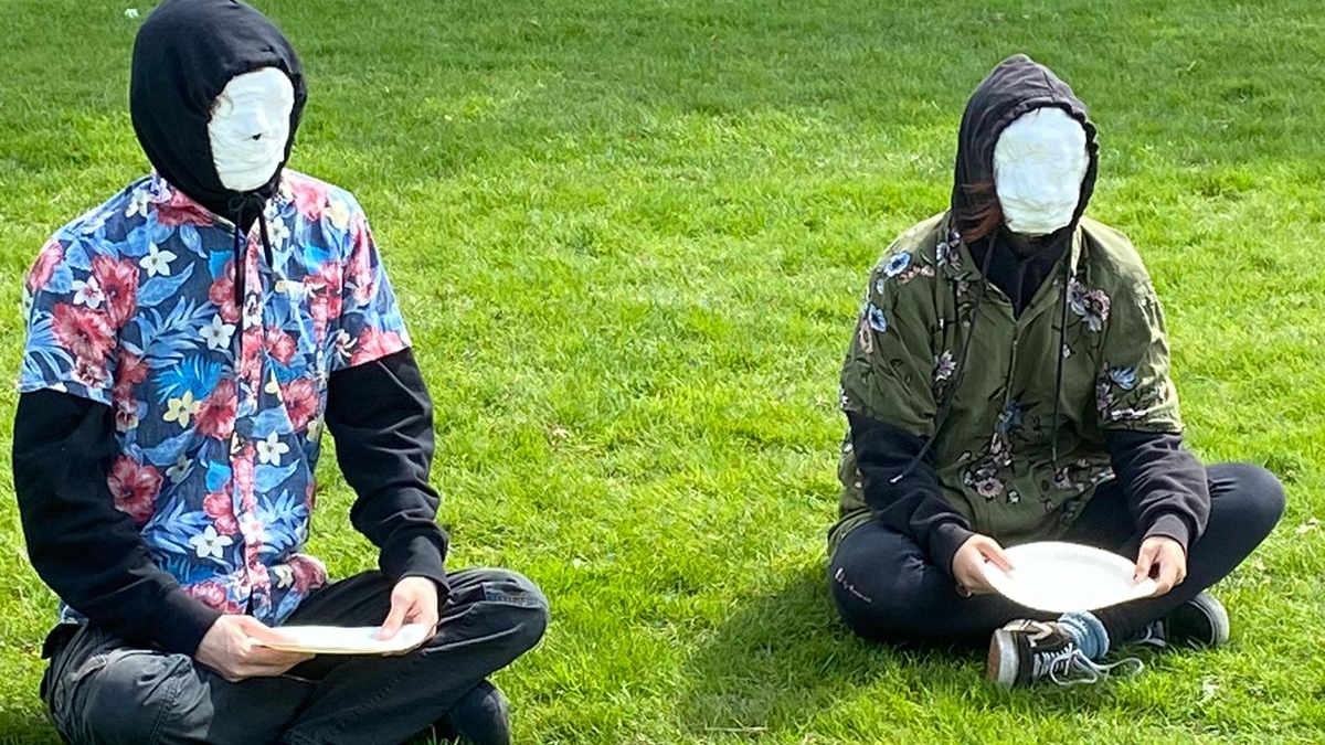 two faceless people in colourful shirts sitting on grass and waiting for food