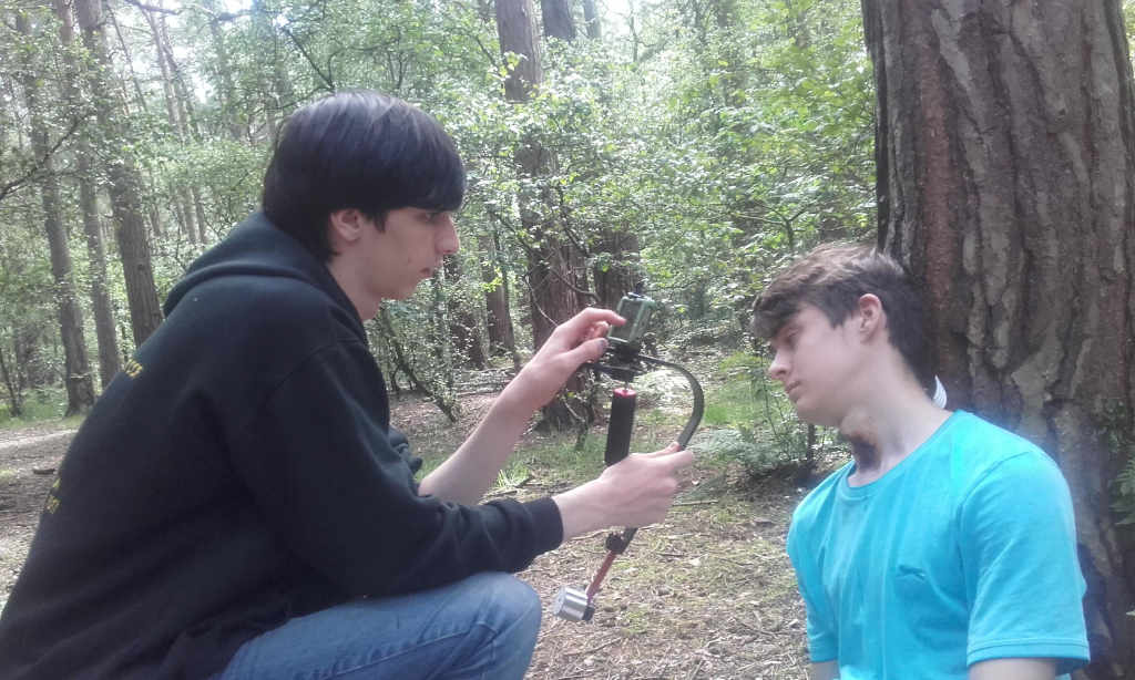 A teenager propped up against a tree being filmed by another teenager