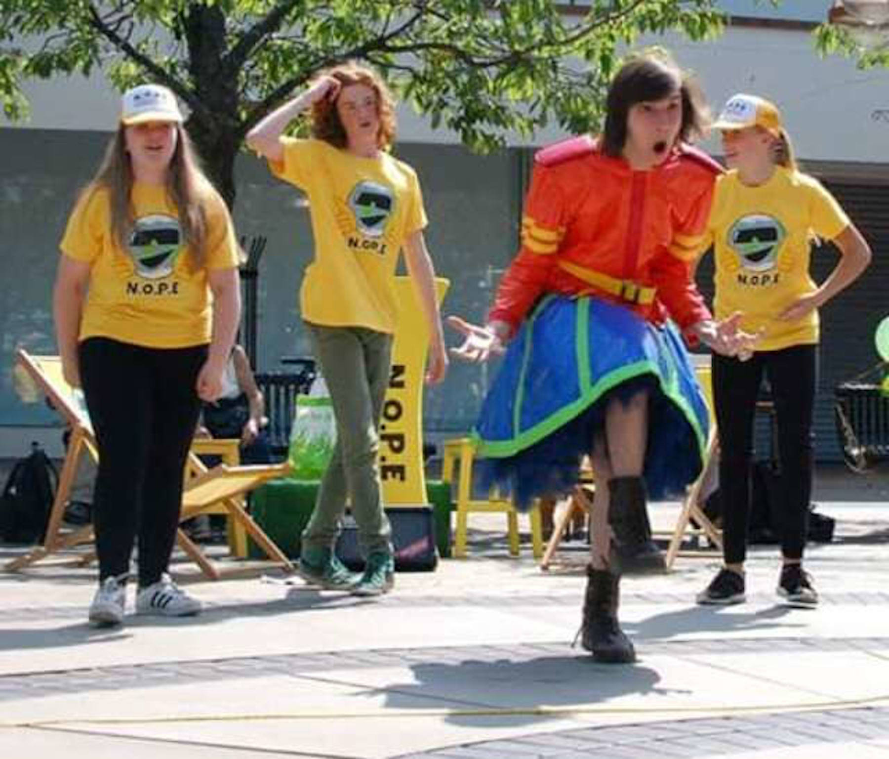 A teenager in a brightly couloured plastic skirt suit dancing in a town centre