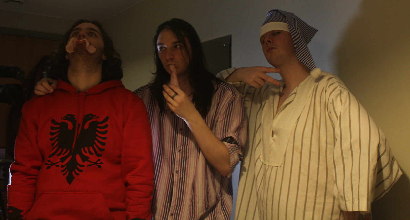 Three men in a dark room. One is in nightwear with a sleeping cap.