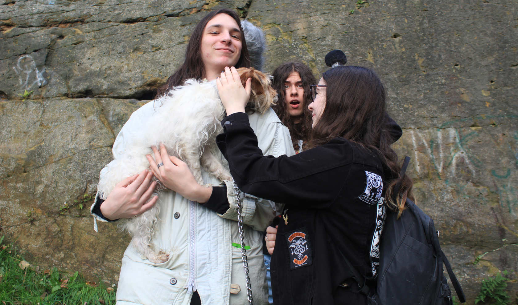 Two men and a woman petting a dog by a cliff