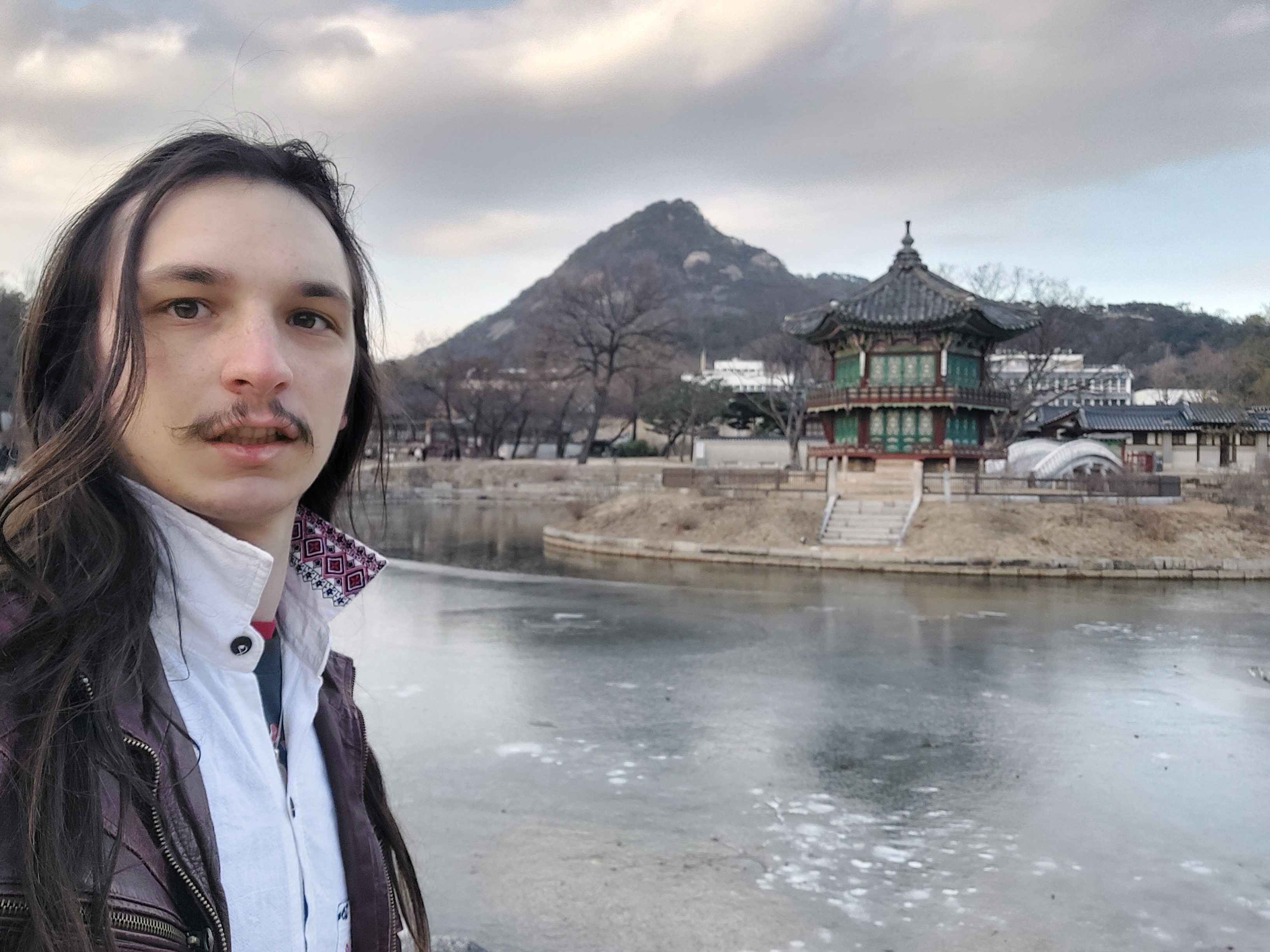A long-haied man leaning against a bridge